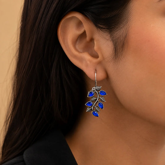 "Blue stone oxidised silver-tone
 leaf earrings with intricate botanical detailing and drop-shaped blue accents, ideal for ethnic, fusion, festive, and everyday wear."
