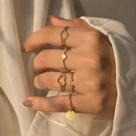 Set of 5 gold-tone dainty charm stacking rings with coin dangle, heart, and wave designs. Western minimal daily wear ring combo for women.
