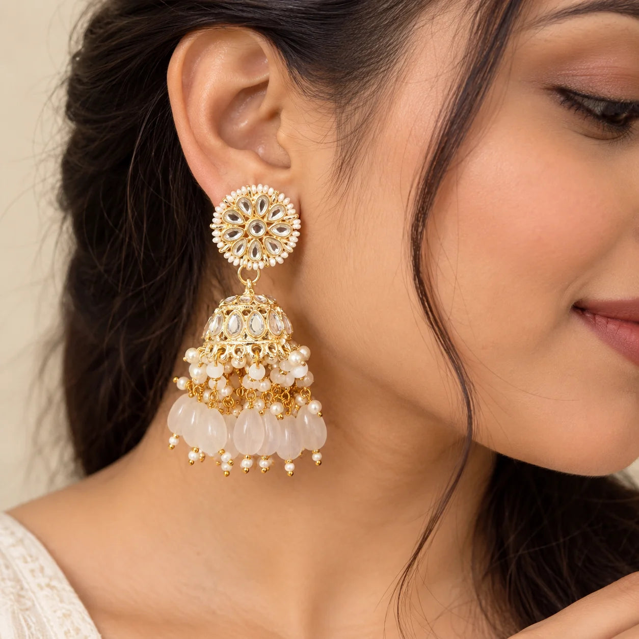 "Gold-toned statement
 jhumka earrings with intricate white stone detailing, layered pearl embellishments, and cascading white bead drops."
