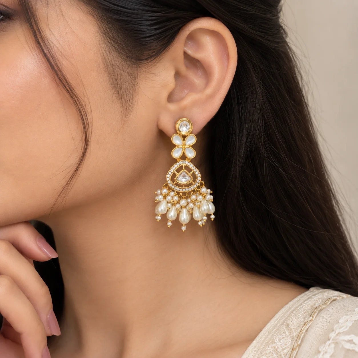 "Gold-toned statement 
earrings with floral white accents, sparkling kundan-style stones, intricate detailing, and cascading white pearl and teardrop bead embellishments."
