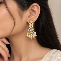 "Gold-toned statement 
earrings with floral white accents, sparkling kundan-style stones, intricate detailing, and cascading white pearl and teardrop bead embellishments."
