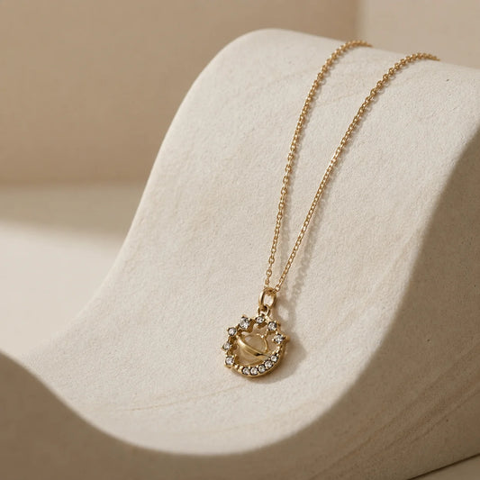 Gold-tone snake chain necklace with mini Saturn planet pendant surrounded by crystal halo. Minimalist celestial jewellery for women.
