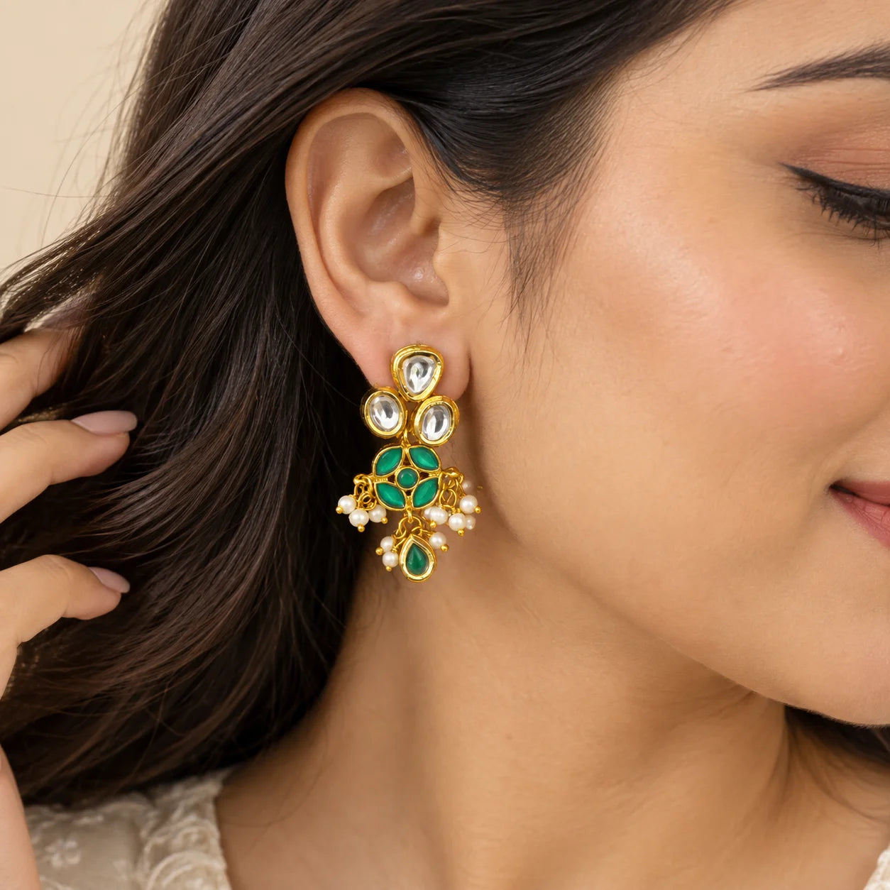 "Gold-toned statement
 earrings with clear Kundan-style stones, vibrant green enamel detailing, delicate white pearl clusters, and green teardrop accents."
