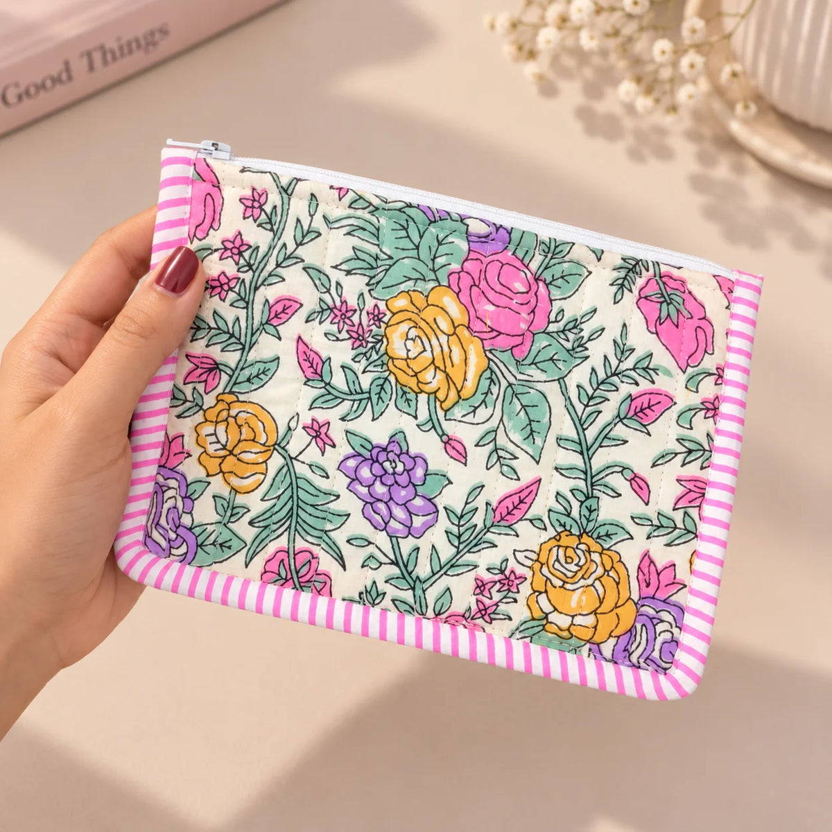 "Colorful floral quilted 
pouch featuring pink, purple, yellow, and green flowers with a pink-and-white striped border and zip closure."
