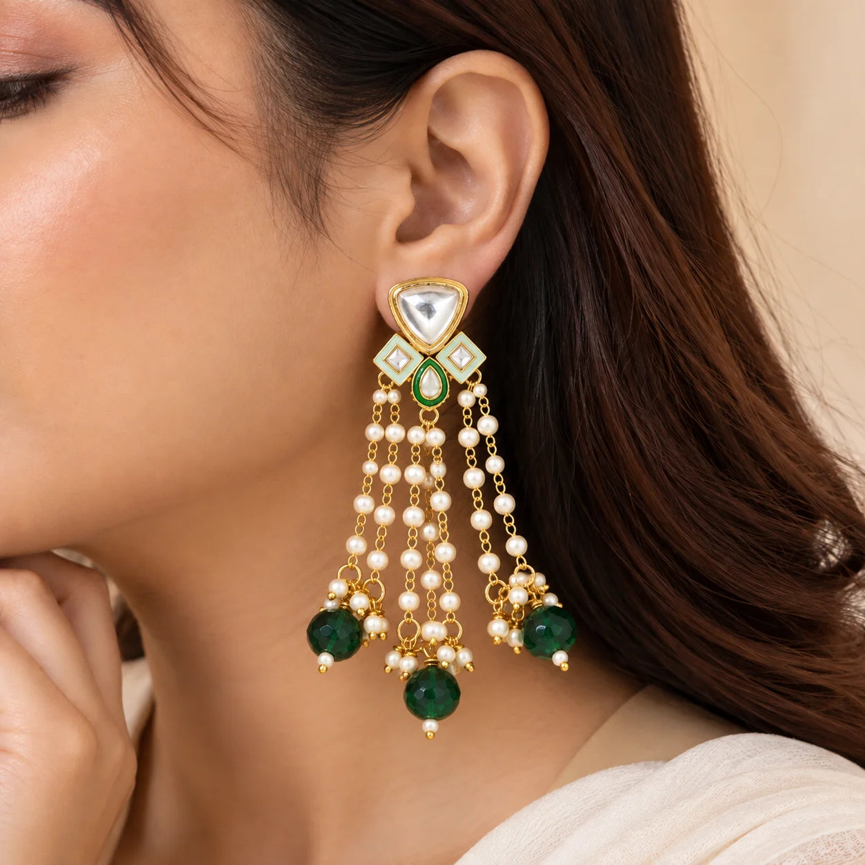"Gold-toned statement 
earrings featuring large clear stones, green accents, intricate geometric detailing, cascading white pearl beads, and deep emerald-green drops."
