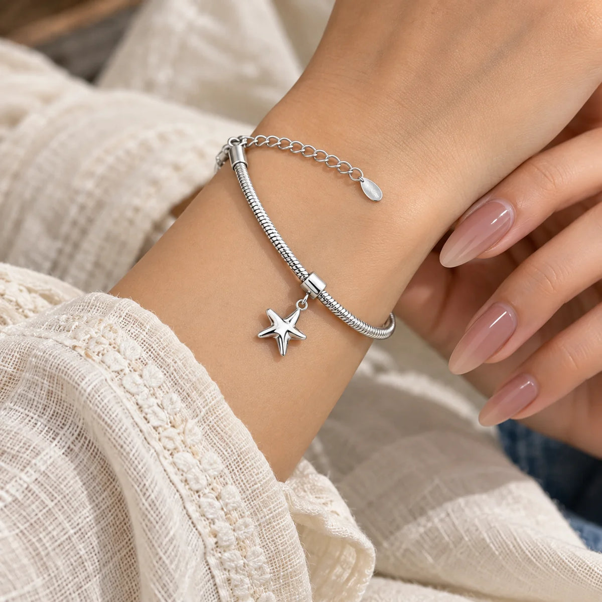 "Silver-toned snake 
chain bracelet featuring a polished five-pointed star charm at the centre, displayed on a wooden surface."
