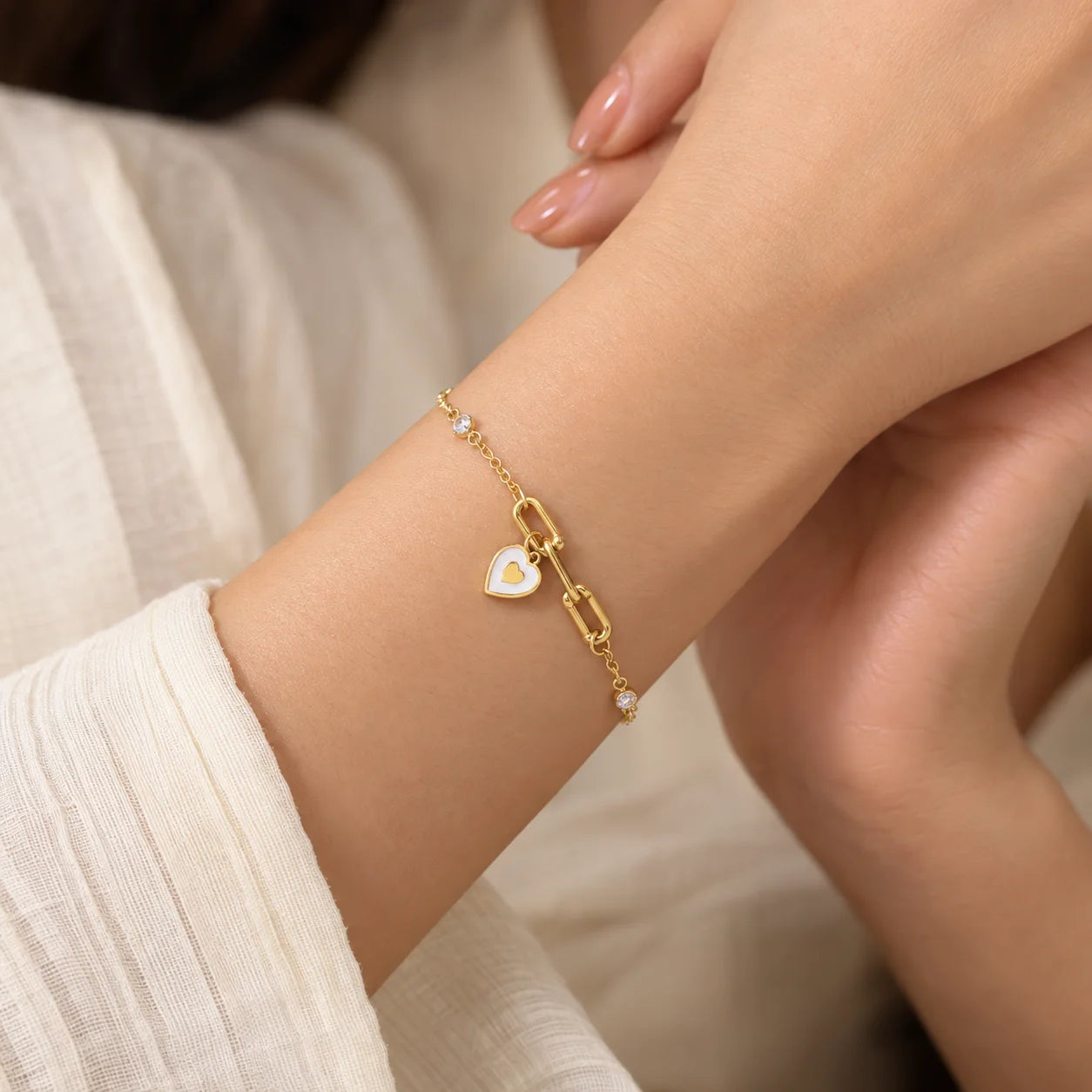 "Gold-toned chain 
bracelet featuring a central bar-link design, small clear bead accents, and a dangling white heart charm with a red heart detail."

