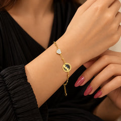 "Delicate gold-toned 
chain bracelet featuring a circular charm with a celestial silhouette and a small sparkling heart charm."
