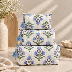 "Set of three quilted fabric 
pouches with a cream-white base, featuring skyblue floral motifs, green leaves, soft blue accents, and decorative blue tassels."
