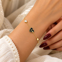"Gold-toned chain bracelet 
featuring a heart-shaped centre charm with a heartbeat design, a small heart accent, and smaller heart charms along the chain."
