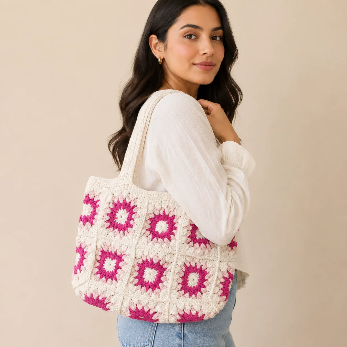 "White crochet shoulder 
bag featuring pink and magenta floral motifs, a textured patchwork design, and long crochet handles."
