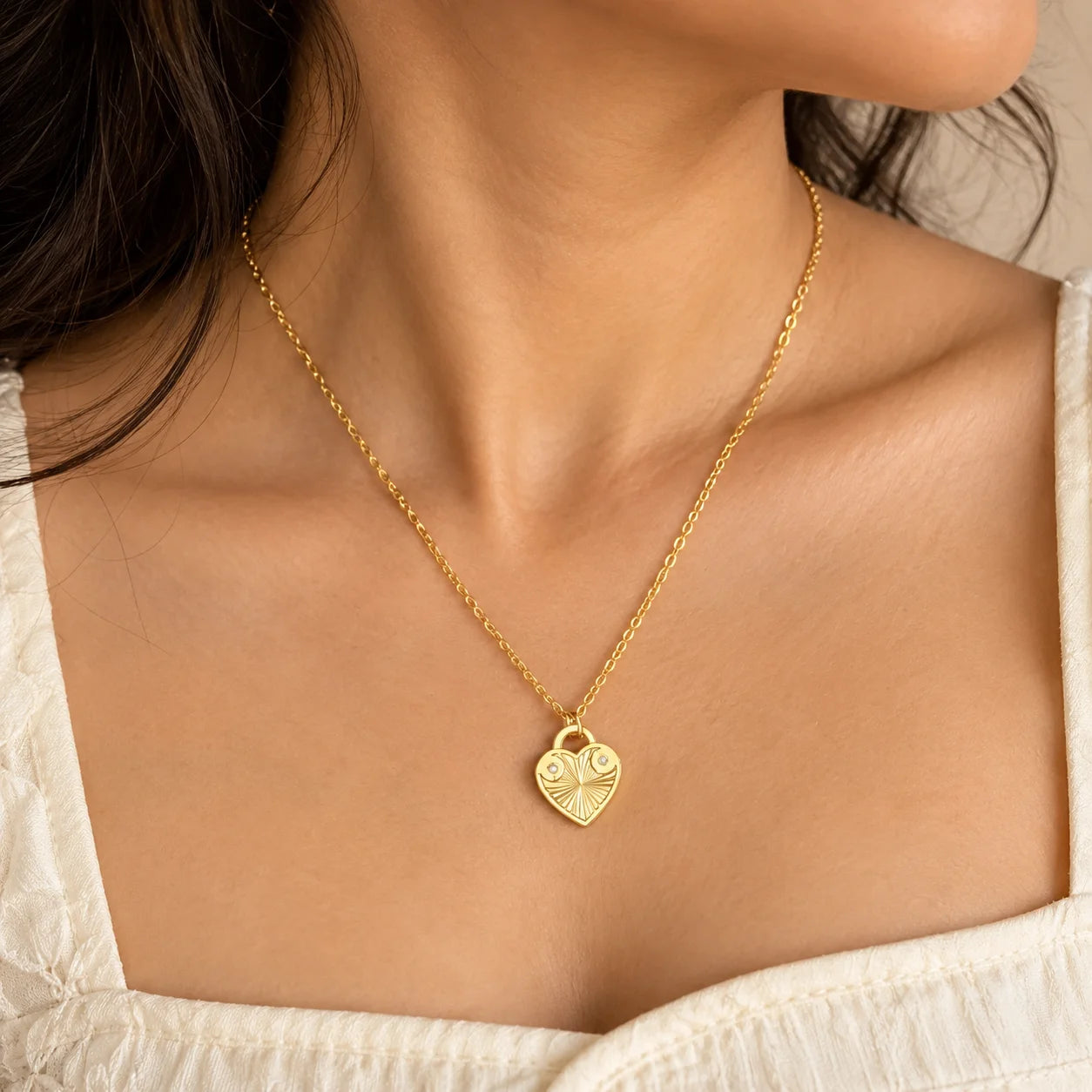 "Gold-toned necklace 
featuring a delicate chain and a heart-shaped pendant with engraved detailing and a radiant sunburst-inspired centre."
