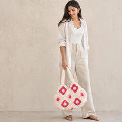 "White crochet shoulder 
bag featuring blush pink and magenta floral granny-square motifs, textured patchwork detailing, and wide crochet straps."
