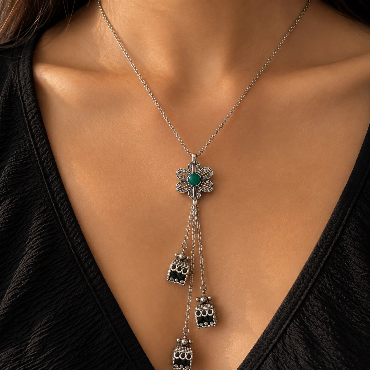 "Oxidised silver-tone necklace
 featuring a floral pendant with a deep green centre stone, intricate detailing, and cascading decorative charms."
