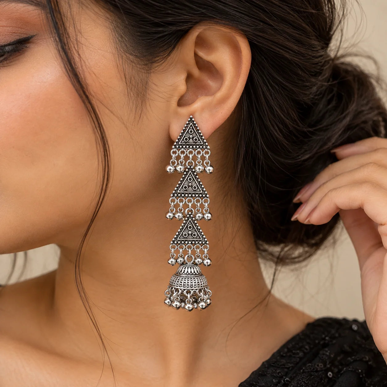 "Silver-toned statement
 earrings featuring three layered triangular panels with intricate detailing, dangling bead accents, and textured dome-shaped jhumka drops."
