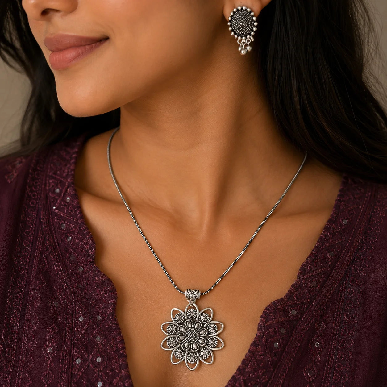 "Oxidised silver-tone
 jewellery set featuring a detailed floral pendant with a matching pair of round drop earrings, all adorned with intricate traditional patterns and small dangling bead accents."
