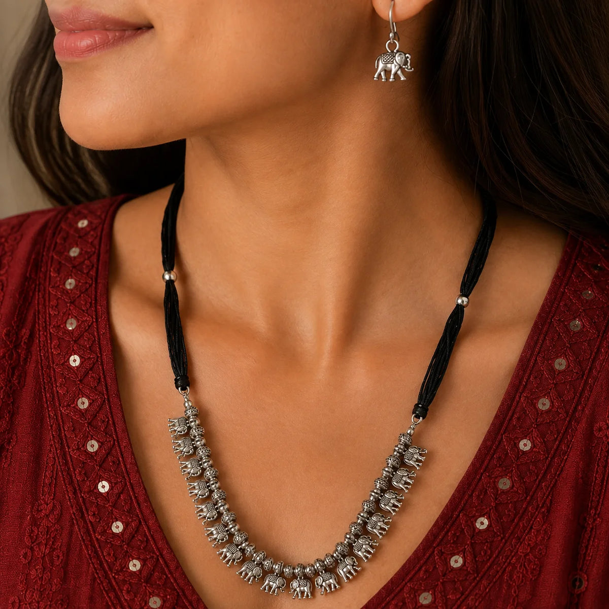 "Oxidised silver-tone necklace
 featuring a row of intricately detailed elephant charms, textured beads, and a black thread tie-up, paired with matching elephant earrings."
