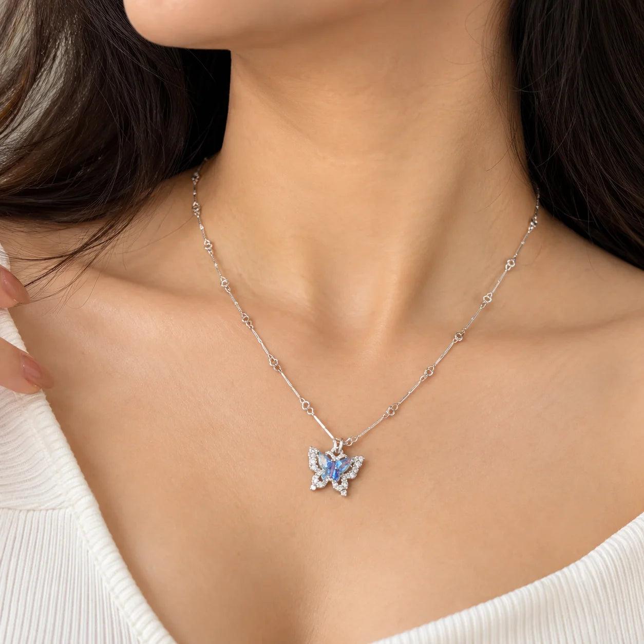 "Delicate silver-toned 
necklace featuring a butterfly pendant with shimmering blue and iridescent stone accents, displayed on a dark background."
