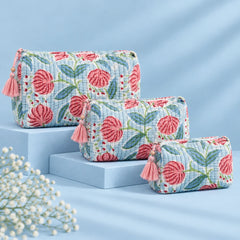 "Set of three quilted
 fabric pouches with a white and grey base, featuring pink floral prints, green leaves, and decorative pink tassel accents."
