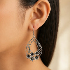 "Oxidised silver-tone teardrop 
earrings featuring intricate cutwork detailing and floral accents in a statement drop design for women."
