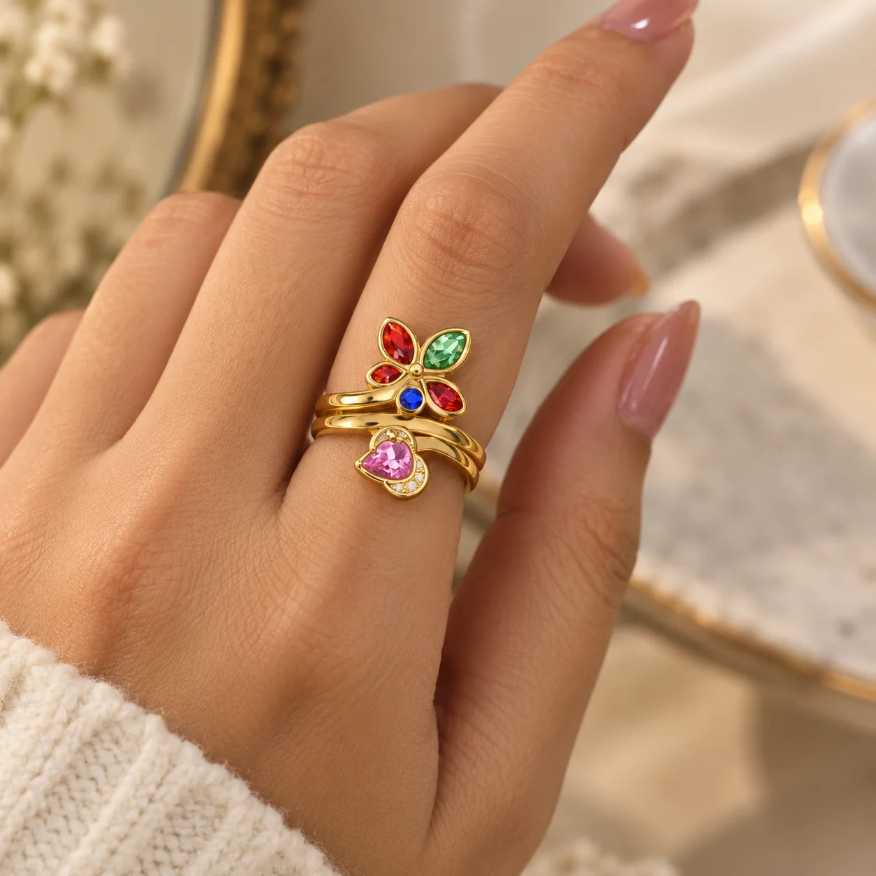 "Gold-toned floral
 ring featuring colourful pastel pink, green, purple, and peach stones in a delicate open vine-inspired design, shown worn on a finger."
