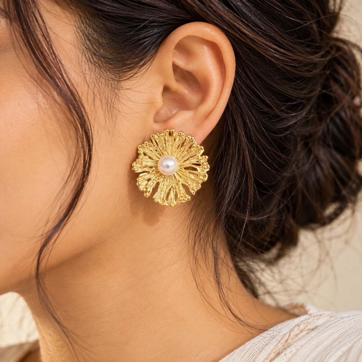 "Gold-toned floral stud
 earrings with intricately textured, layered petals and a round pearl-like centre, displayed on a white earring card."
