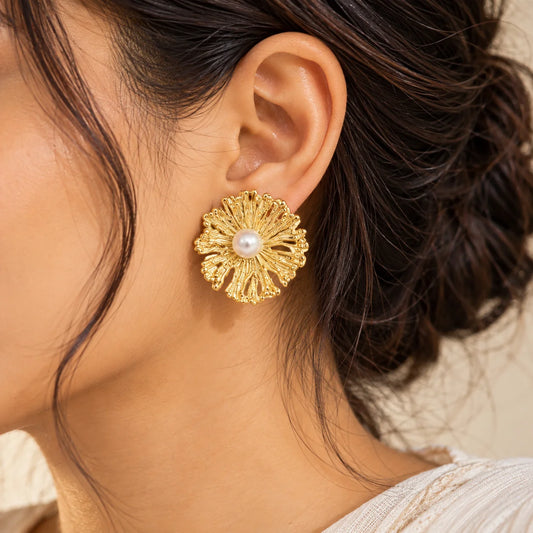 "Gold-toned floral stud
 earrings with intricately textured, layered petals and a round pearl-like centre, displayed on a white earring card."
