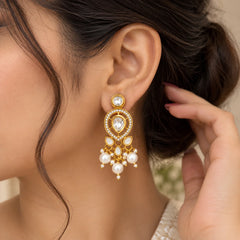 "Gold-toned statement
 earrings featuring teardrop-shaped white stones, sparkling accents, petal-shaped details, and cascading clusters of white pearls."
