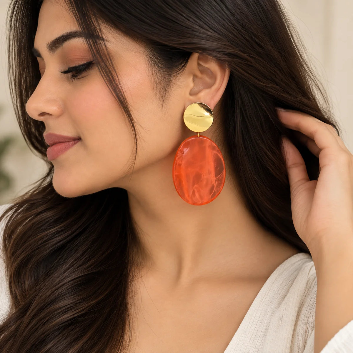 "Orange Drop earrings
 featuring shiny gold-tone round studs and large translucent oval drop pieces in a vibrant coral-orange shade."

