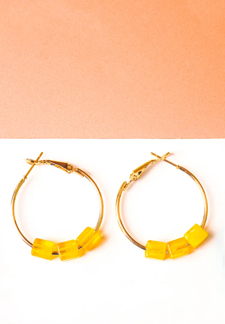 212-TH Chic metal hoop earrings featuring a polished golden-tone finish, playful three translucent yellow cube-shaped beads at the bottom , and a push back for easy wear.