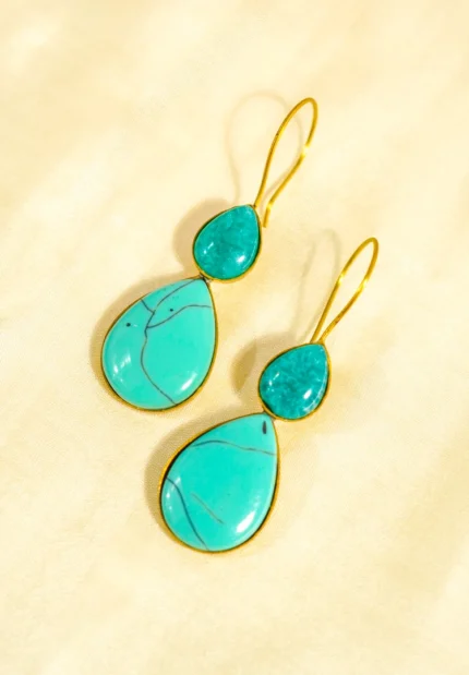 Elegant brass dangle earring with a teardrop shape, adorned with a large turquoise-colored gemstone displaying natural black veining at the bottom. A smaller sea-green turquoise stone sits at the top, secured with a classic curved hook