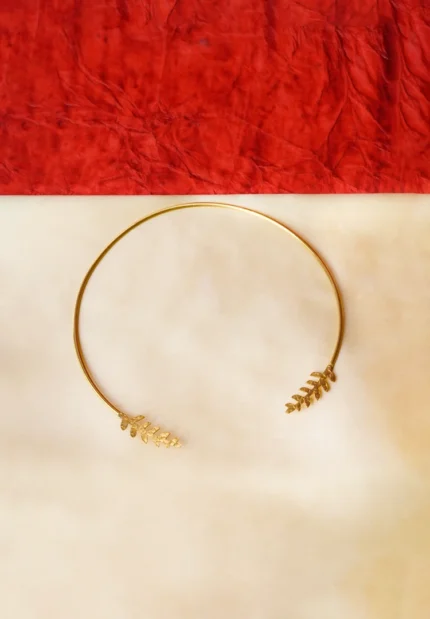 Sleek and sophisticated torque choker necklace in a brushed gold-tone finish, highlighted by hammered-textured leaf-shaped designs gracefully embellishing both ends