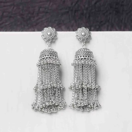 Oxidised jhumka earrings with complex floral detailing, featuring a finely detailedchain tassels, and ghungroos at the bottom, secured with a curved hook closure.