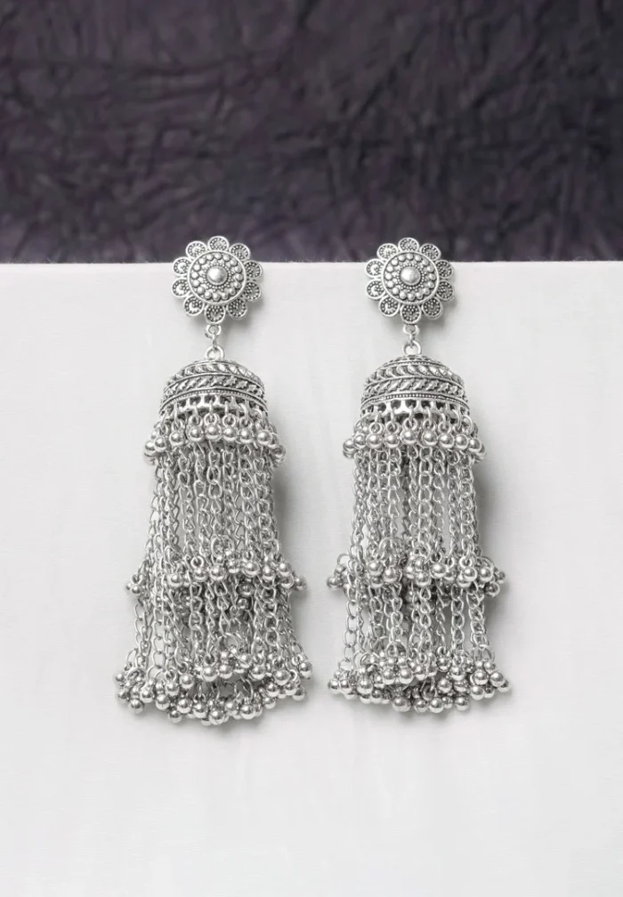 Oxidised jhumka earrings with complex floral detailing, featuring a finely detailedchain tassels, and ghungroos at the bottom, secured with a curved hook closure.
