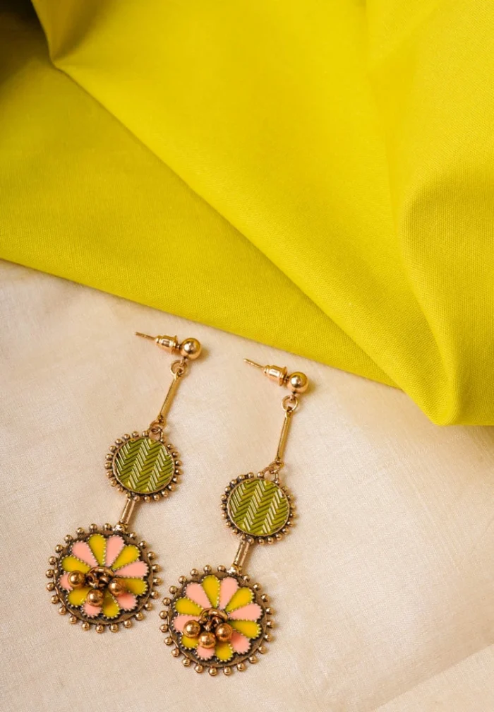 Statement metal drop earrings with an oxidized gold-tone finish, colored top disc, floral-patterned bottom disc, peach and yellow enamel detailing, and a push-back closure
