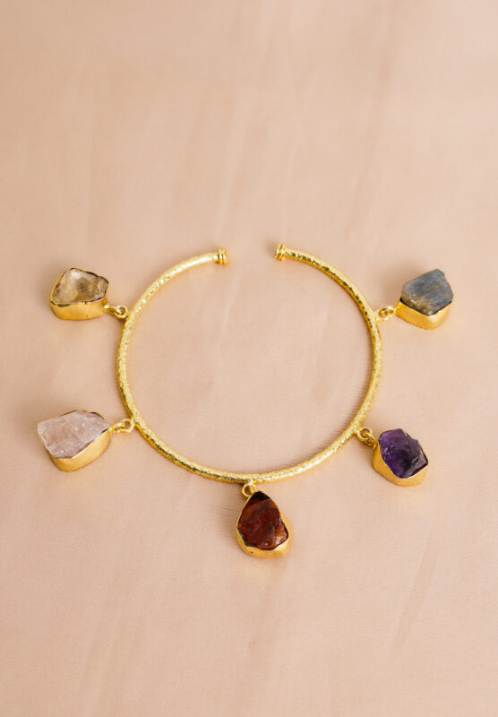 rtistic metal cable bracelet featuring a hammered texture, golden/multicolor sheen, and colorful organic-shaped raw gemstone dangles