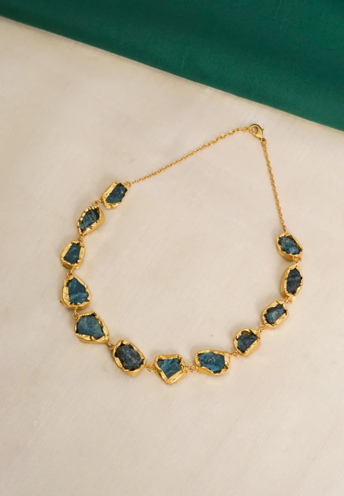 Flat cable chain choker necklace with a polished golden tone/emerald finish, featuring evenly spaced irregular organic-shaped purple raw gemstones and a lobster claw clasp