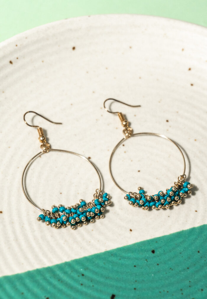 Chic metal hoop earrings featuring a polished gold-tone finish, playful turquoise enamel accents, also mini beads and a push back for easy wear