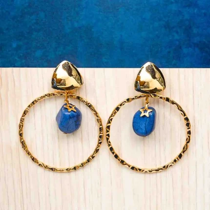 Chic metal hoop earrings featuring a polished gold-tone finish, dangling blue assymetrical stone, a golden charm and, a push back for easy wear.