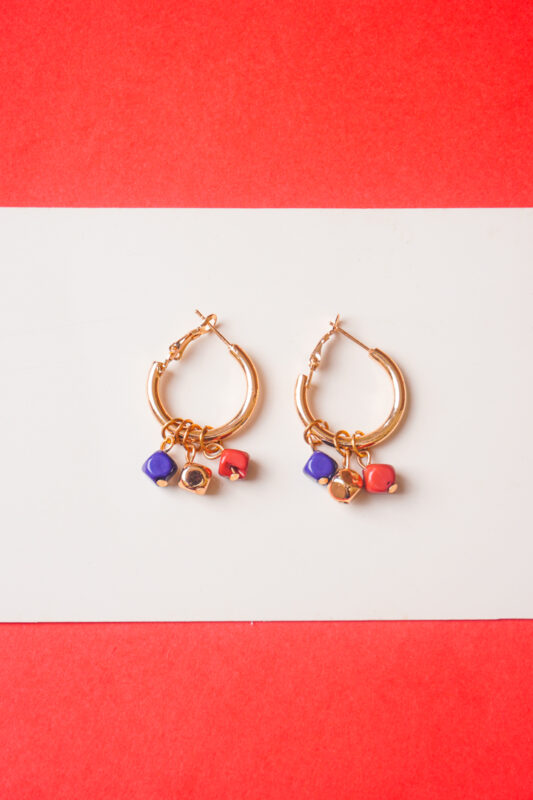 Chic metal hoop earrings featuring a polished gold-toneburnt umber finish featuring golden blue and brick coloured mini cube shaped chrams at the bottom, and a hinged back for easy wear.