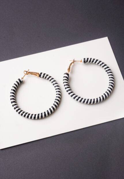 Chic metal hoop earrings featuring a polished gold-tone finish, playful black and white stripped patterned thread , and a golden hinged for easy wear.