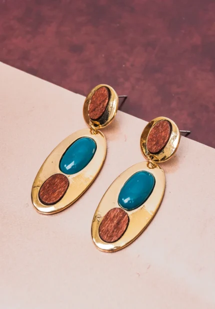Eye-catching oval-shaped drop earrings with a luxe gold-tone finish, a deep teal stone at the center, and two organic wooden detailing, secured with a push-back post.
