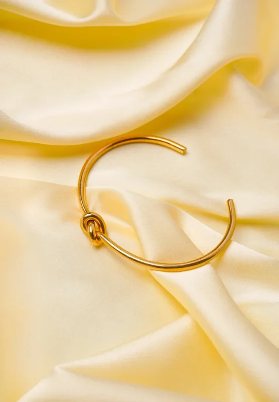 Polished gold-tone open bangle featuring a sleek and minimal knot detail, perfect for an elegant and understated look
