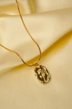 Sophisticated gold-tone snake chain necklace with a slightly irregular framed oval pendant, adorned with an embossed flower motif, complete with a lobster claw closure.