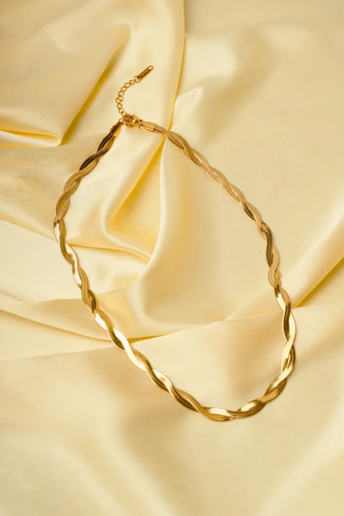 Sophisticated gold-tone snake chain necklace with a slightly irregular framed oval pendant, adorned with an embossed flower motif, complete with a lobster claw closure