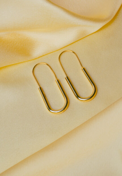 Refined gold-tone elongated oval metal hoop earrings with a pin structure and a lever back closure.