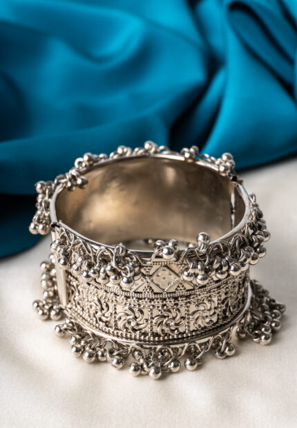 Oxidized silver-tone metal cuff bracelet featuring fine intricate detailing and adorned with ghungroos on both edges