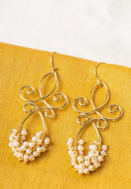 Polished gold-tone/pearl white dangle earring with an elegant looped pattern, fine intricate detailing, and delicate small pearl bead embellishments, secured with a French hook closure.