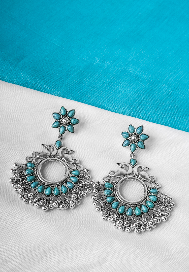 496-Th Metal dangle earring with oxidised silver tone finish featuring bird shaped design with flower shaped top designed with turquoise coloured teardrop shaped stones and ghungroos with a curved hook closure