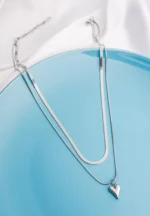 Modern two layered snake chain necklace with a polished silver finish, a solid heart charm, and an adjustable lobster clasp.